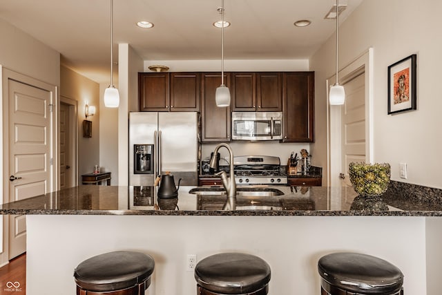 kitchen featuring dark brown cabinetry, a breakfast bar, dark stone countertops, appliances with stainless steel finishes, and a sink