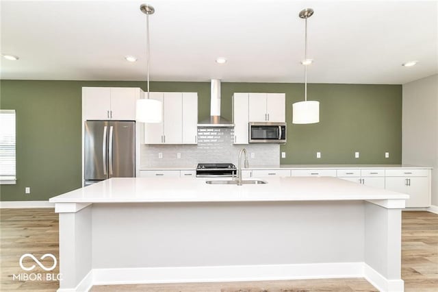 kitchen featuring a sink, stainless steel appliances, white cabinets, light wood-style floors, and wall chimney range hood