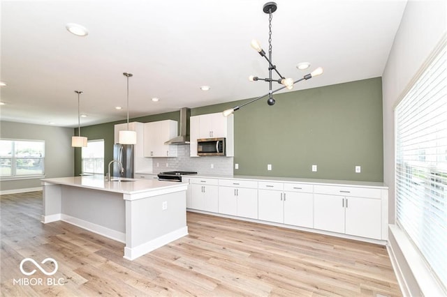 kitchen featuring stainless steel microwave, light wood-style floors, white cabinetry, wall chimney exhaust hood, and a sink