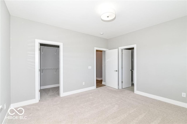 unfurnished bedroom featuring baseboards, light carpet, a closet, and a spacious closet