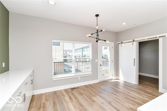 unfurnished dining area with a barn door, light wood-style flooring, a notable chandelier, and baseboards