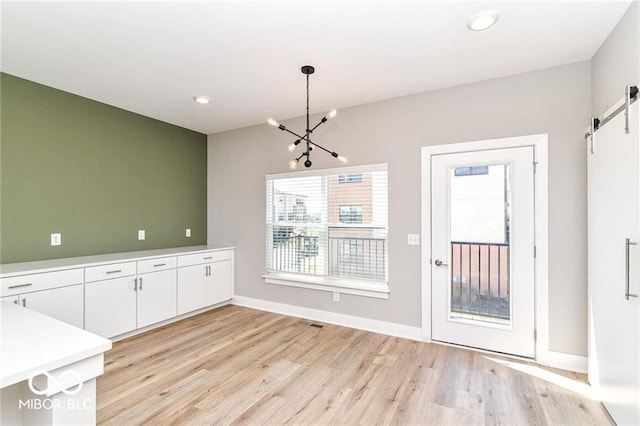 unfurnished dining area with baseboards, light wood-style flooring, recessed lighting, a barn door, and a chandelier