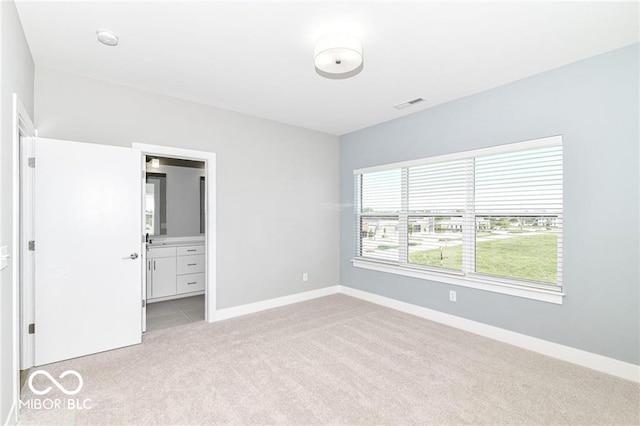 unfurnished bedroom with light colored carpet, visible vents, ensuite bathroom, and baseboards