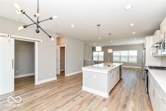 kitchen featuring a sink, stainless steel appliances, light wood-style floors, and an island with sink