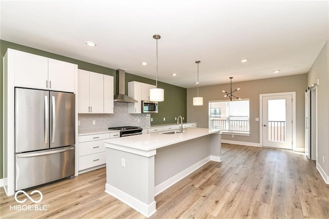 kitchen featuring white cabinets, stainless steel appliances, wall chimney range hood, and a sink