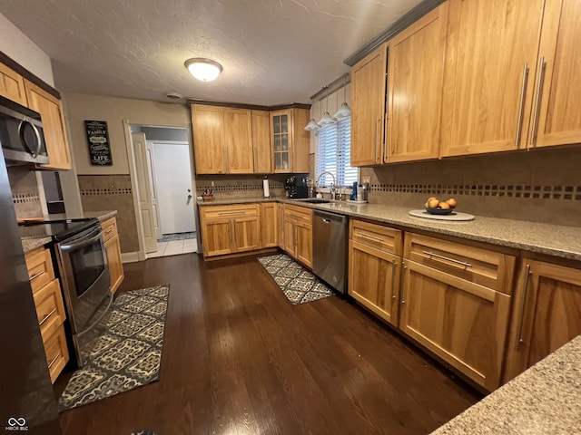 kitchen with decorative backsplash, a sink, stainless steel appliances, glass insert cabinets, and dark wood-style flooring