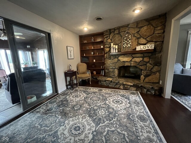 sitting room with visible vents, built in features, a stone fireplace, and wood finished floors