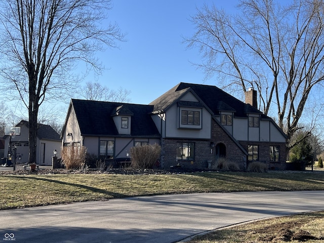 tudor home with a front yard, a chimney, and stucco siding