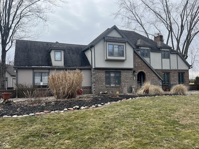 tudor home with brick siding, a shingled roof, a front yard, stucco siding, and a chimney