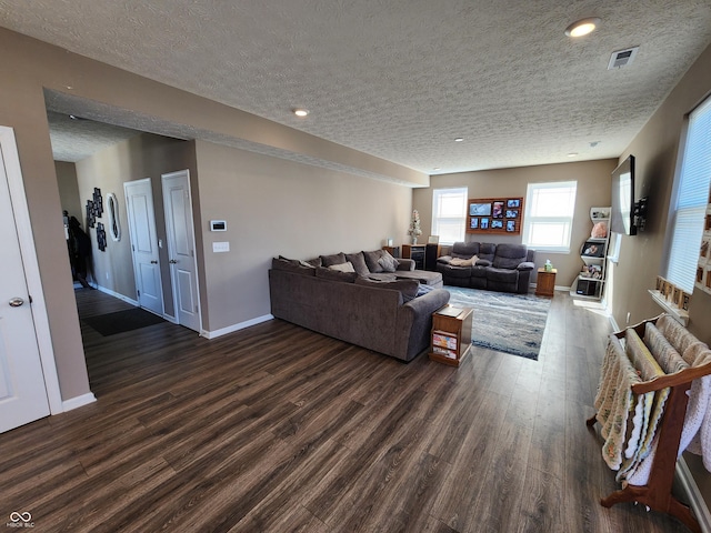 living area with visible vents, baseboards, a textured ceiling, and dark wood finished floors