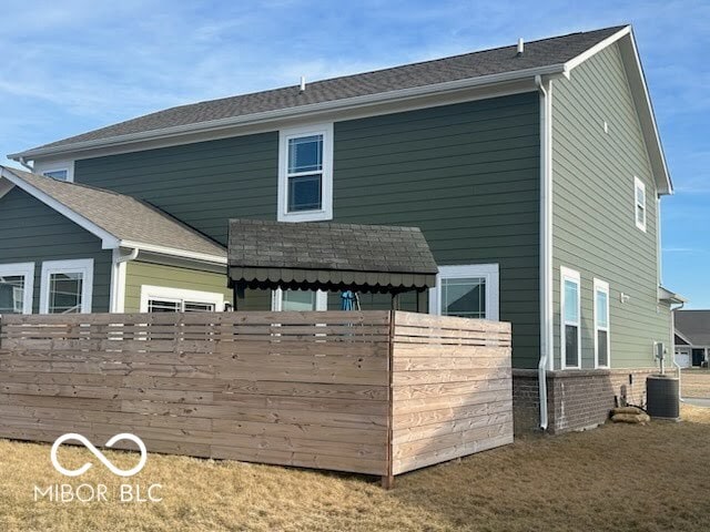 rear view of property with fence, brick siding, and central AC