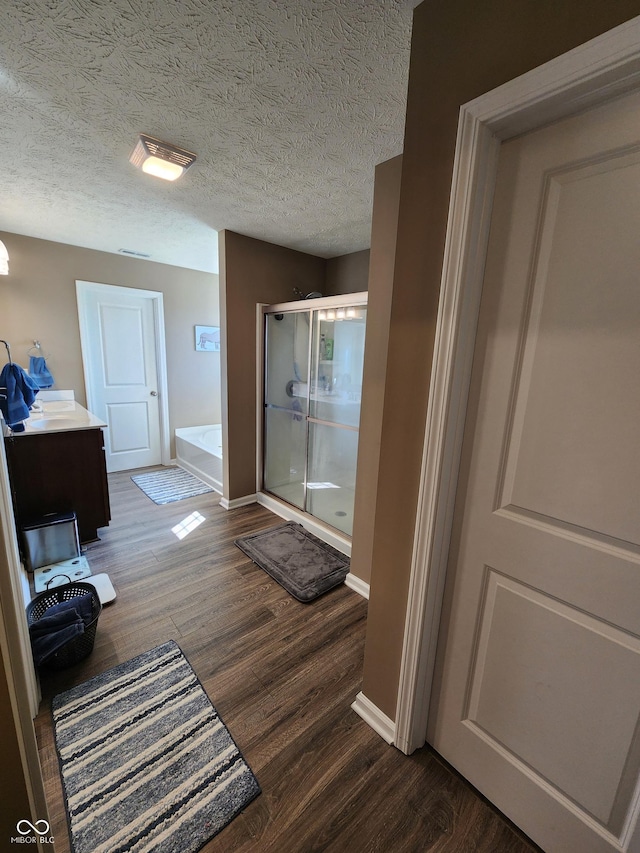 full bathroom featuring a bath, a stall shower, baseboards, and wood finished floors