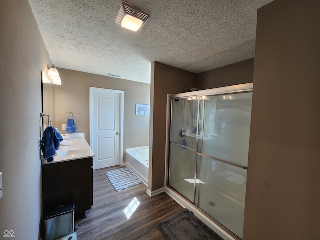 bathroom with a garden tub, double vanity, a stall shower, wood finished floors, and a textured ceiling