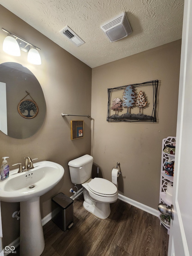 half bath featuring toilet, wood finished floors, visible vents, and a textured ceiling