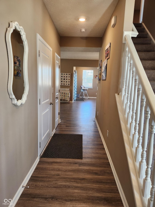 corridor featuring stairway, a textured ceiling, baseboards, and dark wood-style flooring