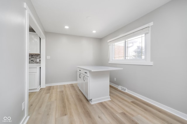 kitchen featuring light wood finished floors, decorative backsplash, light countertops, and baseboards