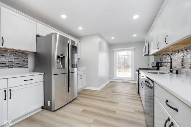 kitchen with a sink, tasteful backsplash, white cabinetry, stainless steel appliances, and light wood-style floors