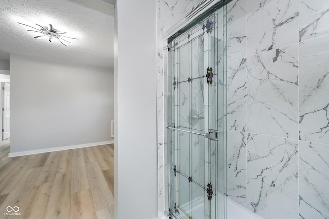 full bath with baseboards, a textured ceiling, and wood finished floors