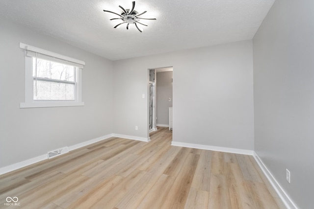 spare room featuring a textured ceiling, light wood-style floors, visible vents, and baseboards