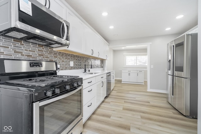 kitchen featuring light wood-type flooring, light countertops, stainless steel appliances, white cabinetry, and a sink