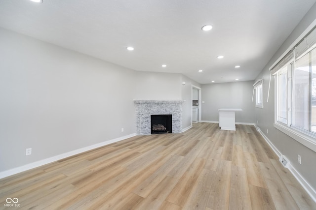 unfurnished living room featuring a stone fireplace, recessed lighting, baseboards, and light wood finished floors