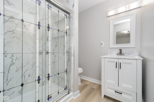 bathroom featuring vanity, wood finished floors, baseboards, a shower stall, and toilet