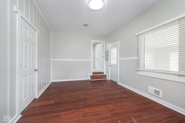 corridor with baseboards, wood finished floors, visible vents, and a textured ceiling