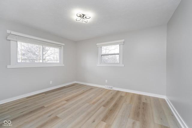 unfurnished room featuring visible vents, baseboards, light wood-style floors, and a textured ceiling