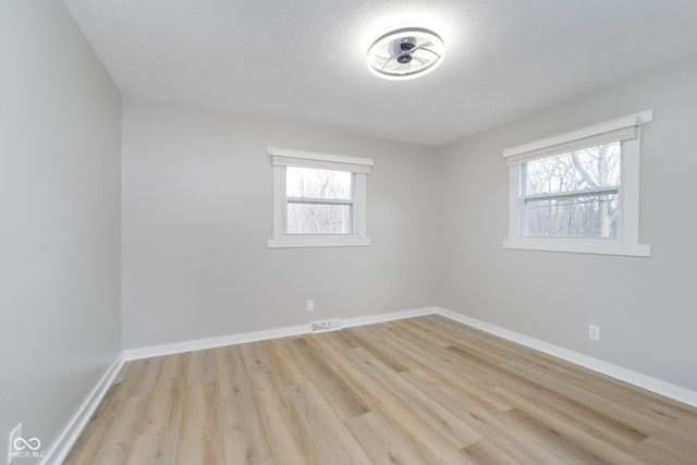 spare room featuring wood finished floors, a healthy amount of sunlight, visible vents, and baseboards