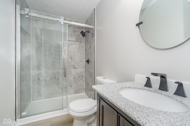 full bathroom with toilet, a stall shower, vanity, and a textured ceiling