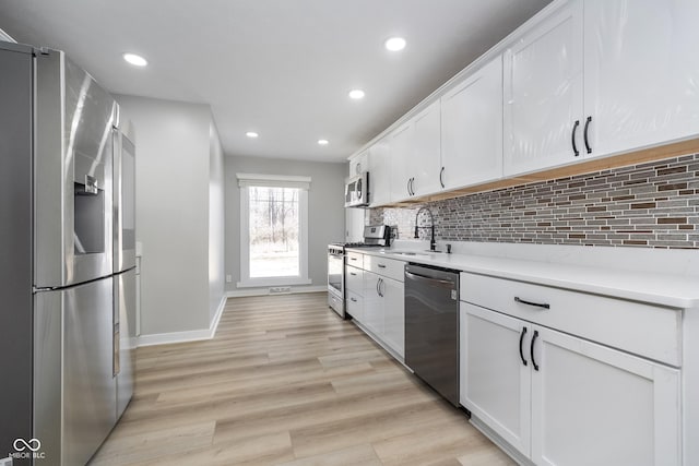 kitchen featuring light wood-style flooring, a sink, stainless steel appliances, white cabinets, and decorative backsplash