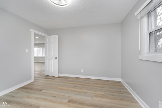 empty room with baseboards, a textured ceiling, and light wood-style flooring