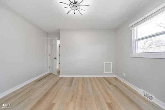 spare room with visible vents, a textured ceiling, light wood-type flooring, and baseboards