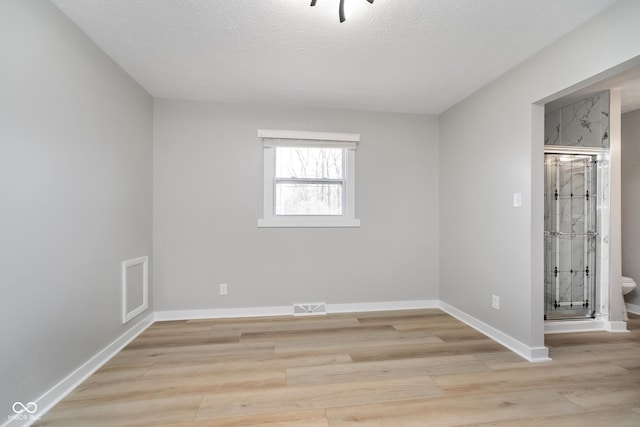 empty room with light wood-type flooring, visible vents, baseboards, and a textured ceiling