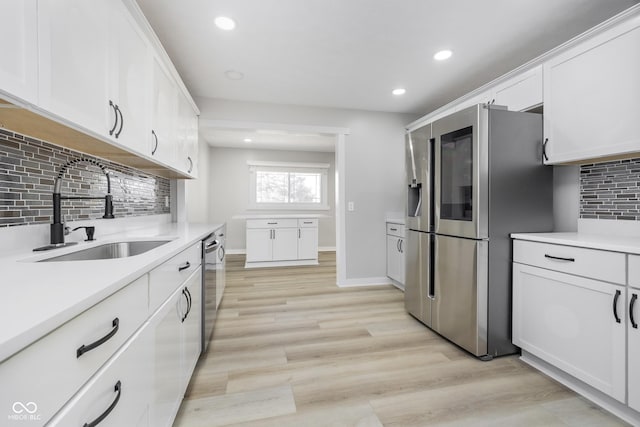 kitchen with light countertops, appliances with stainless steel finishes, light wood-style floors, white cabinetry, and a sink