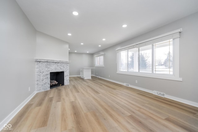 unfurnished living room featuring visible vents, baseboards, a fireplace, and light wood finished floors