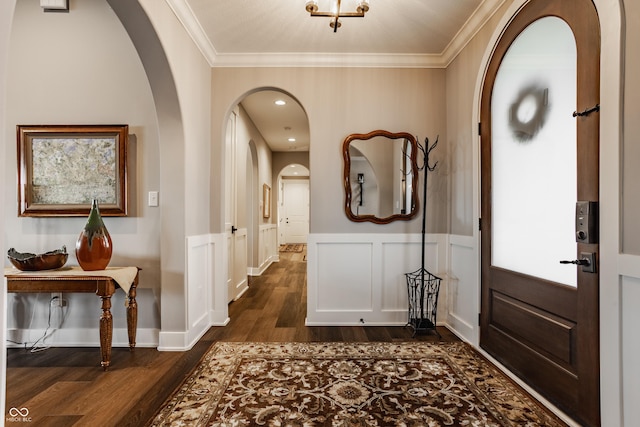 entryway with ornamental molding, arched walkways, wainscoting, a decorative wall, and dark wood-style flooring