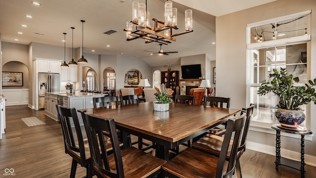 dining space with visible vents, arched walkways, a stone fireplace, and dark wood finished floors