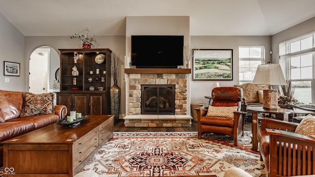 living room featuring arched walkways, a stone fireplace, and wood finished floors