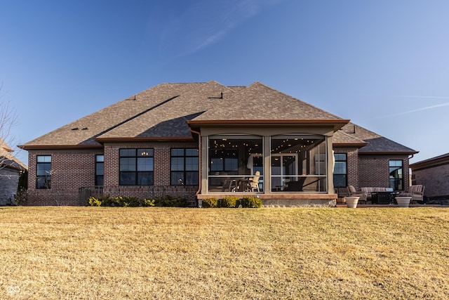 rear view of house featuring a lawn, brick siding, a sunroom, and a shingled roof