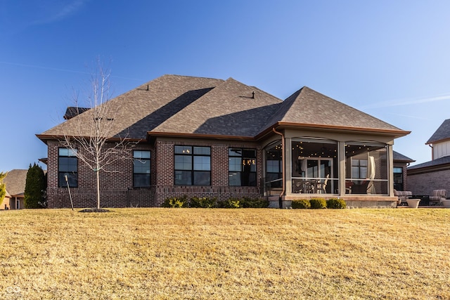 rear view of property featuring a yard, brick siding, a sunroom, and a shingled roof