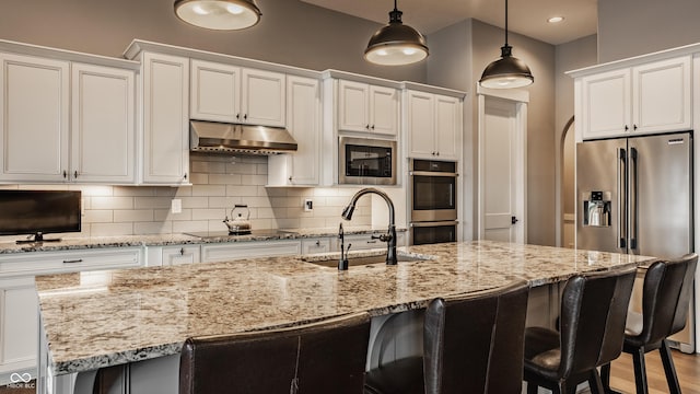 kitchen featuring under cabinet range hood, a sink, backsplash, white cabinetry, and stainless steel appliances