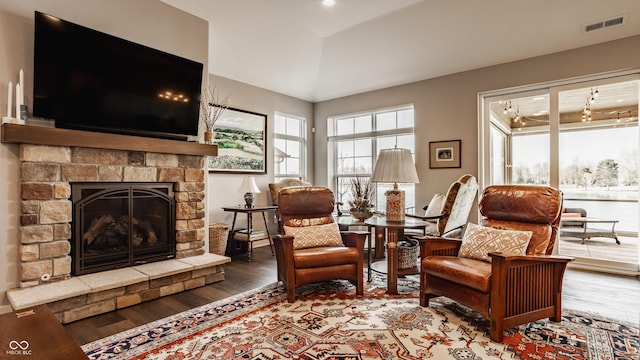 living area with visible vents, a stone fireplace, and wood finished floors