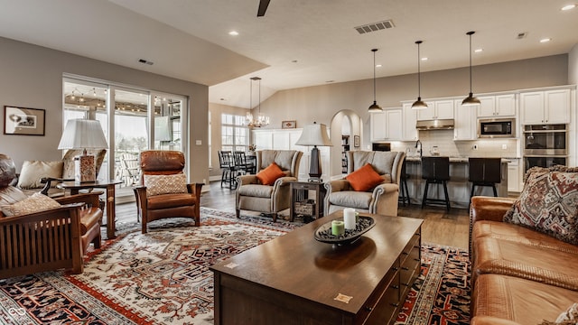 living room with a notable chandelier, visible vents, vaulted ceiling, and wood finished floors