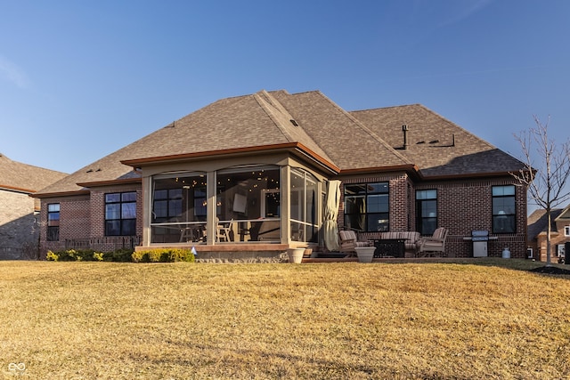 back of property with a lawn, brick siding, a sunroom, and roof with shingles