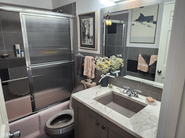 full bathroom with vanity, tile walls, toilet, combined bath / shower with glass door, and backsplash