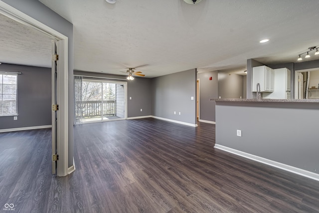 unfurnished living room with a wealth of natural light, baseboards, and dark wood-type flooring