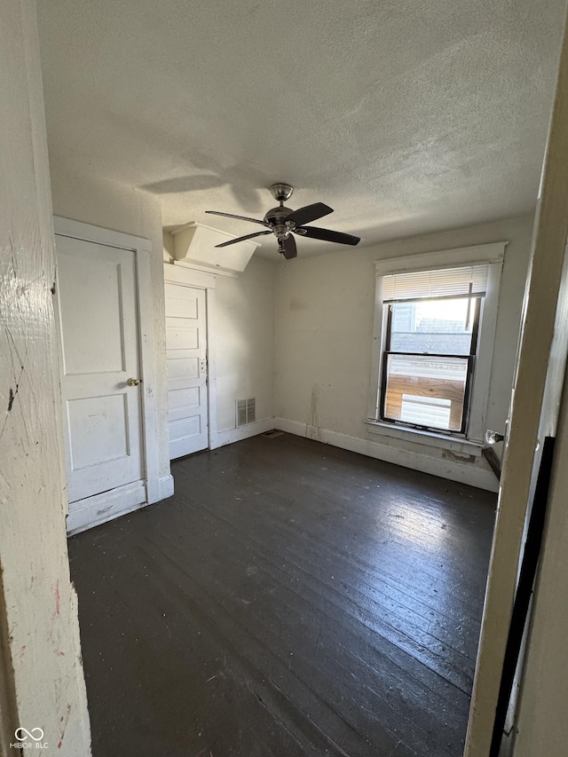 spare room with a ceiling fan, baseboards, visible vents, dark wood-type flooring, and a textured ceiling