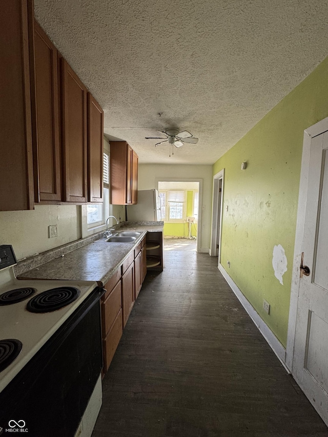 kitchen with electric stove, a sink, a textured ceiling, dark wood-style floors, and baseboards