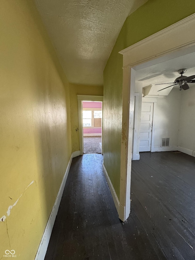 hall with visible vents, a textured ceiling, baseboards, and hardwood / wood-style floors